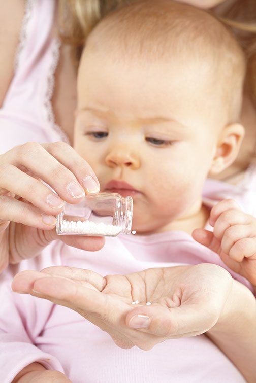 Homöopathie für Babys: Mutter gibt homöopathische Globuli auf dem Schoss ihres Säuglings
