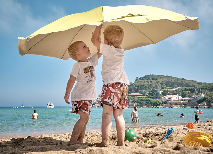 2 Kleinkinder stellen einen Sonnenschirm am Strand auf